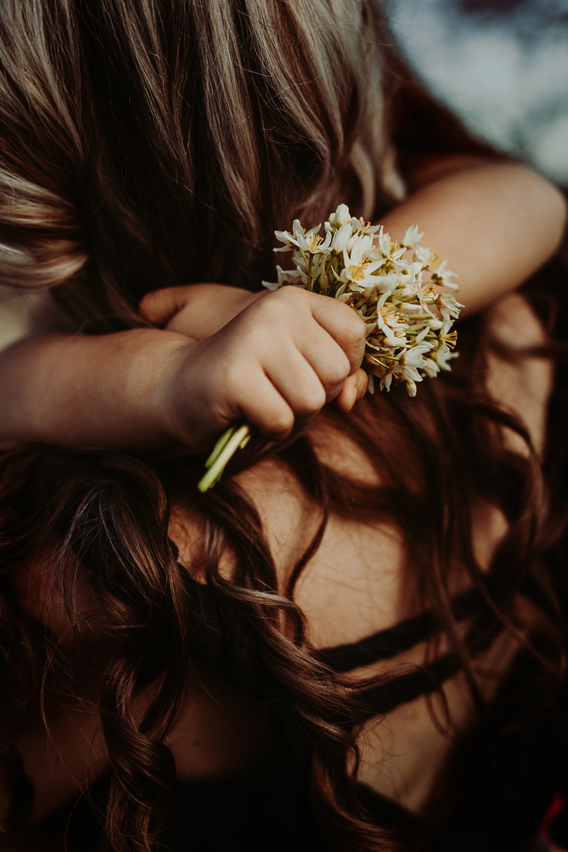 young child hugging mother while holding wild flowers